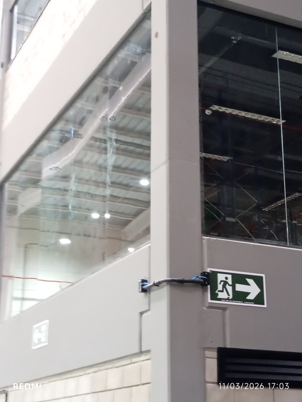 Eletroduto, caixa de passagem e placa de saída de emergência em coluna de galpão