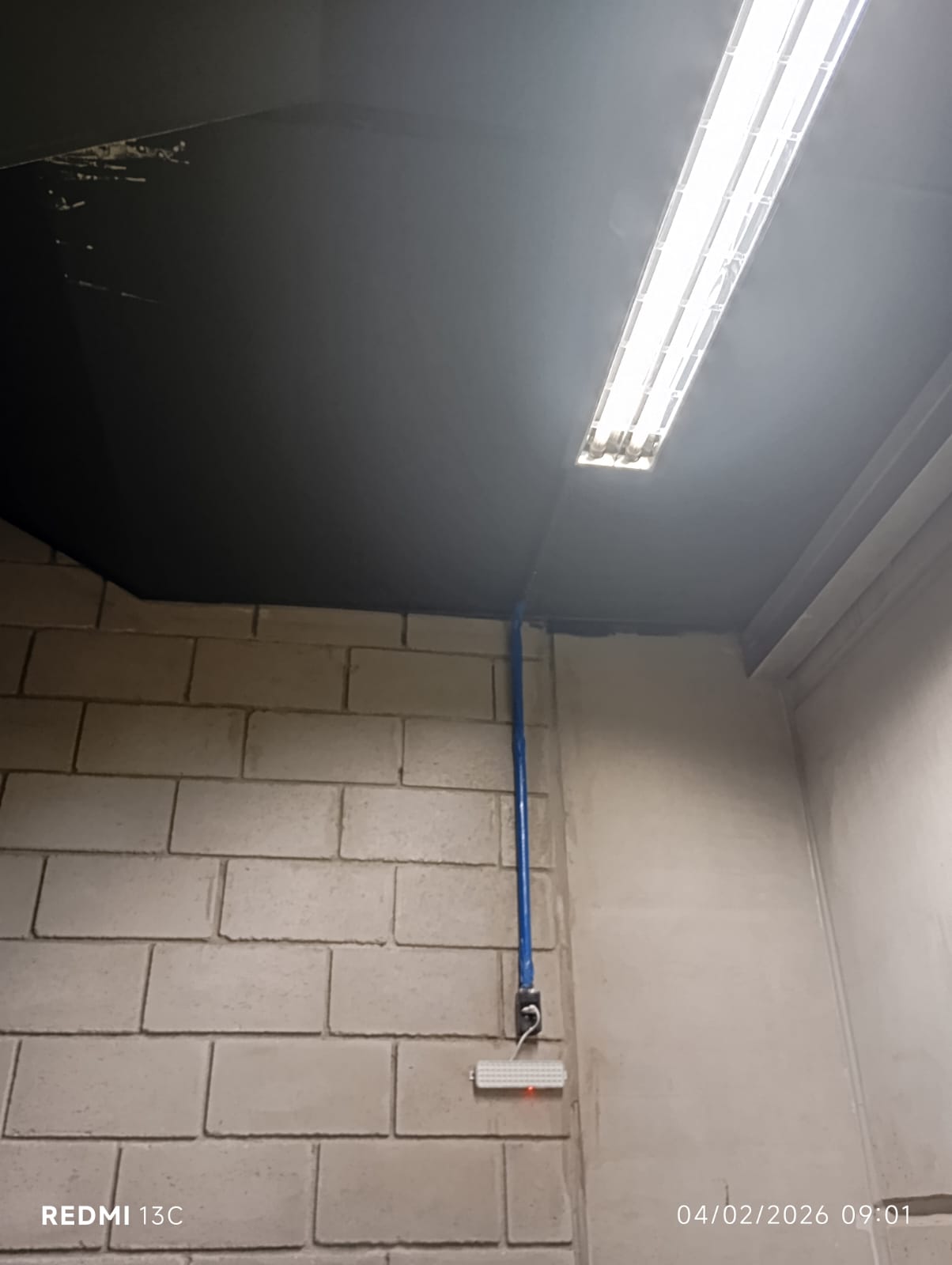Luminária, eletroduto azul e luz de emergência instalados em parede